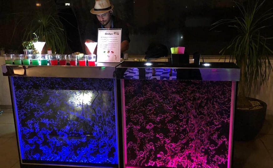 Bartender com balcão iluminado servindo drinks coloridos em festa de Halloween