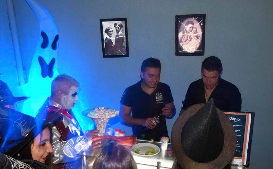 Convidados fantasiados em festa de Halloween com quadros assustadores na parede